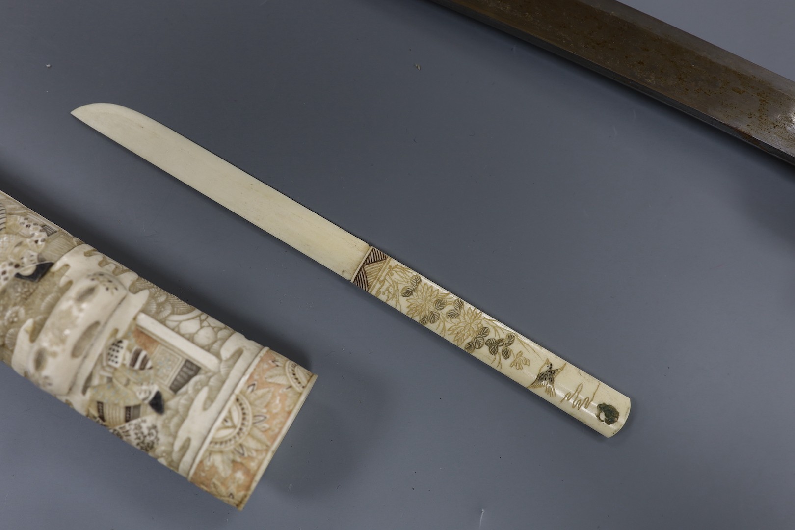 A Japanese carved and coloured ivory tanto, Meiji period, the hilt and scabbard carved to both sides with figures in ceremonial dress, the whole etched in black , green and red, the separate kodzuka with ivory blade and